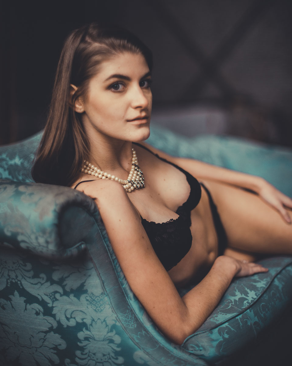 Richmond boudoir photography photo of brunette woman in black lingerie wearing a pearl necklace reclining on a teal blue couch