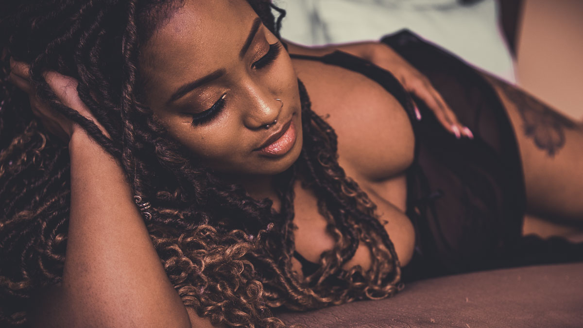 Richmond boudoir photography maternity photo of pregnant black woman in black lingerie laying on her side on a brown bedspread