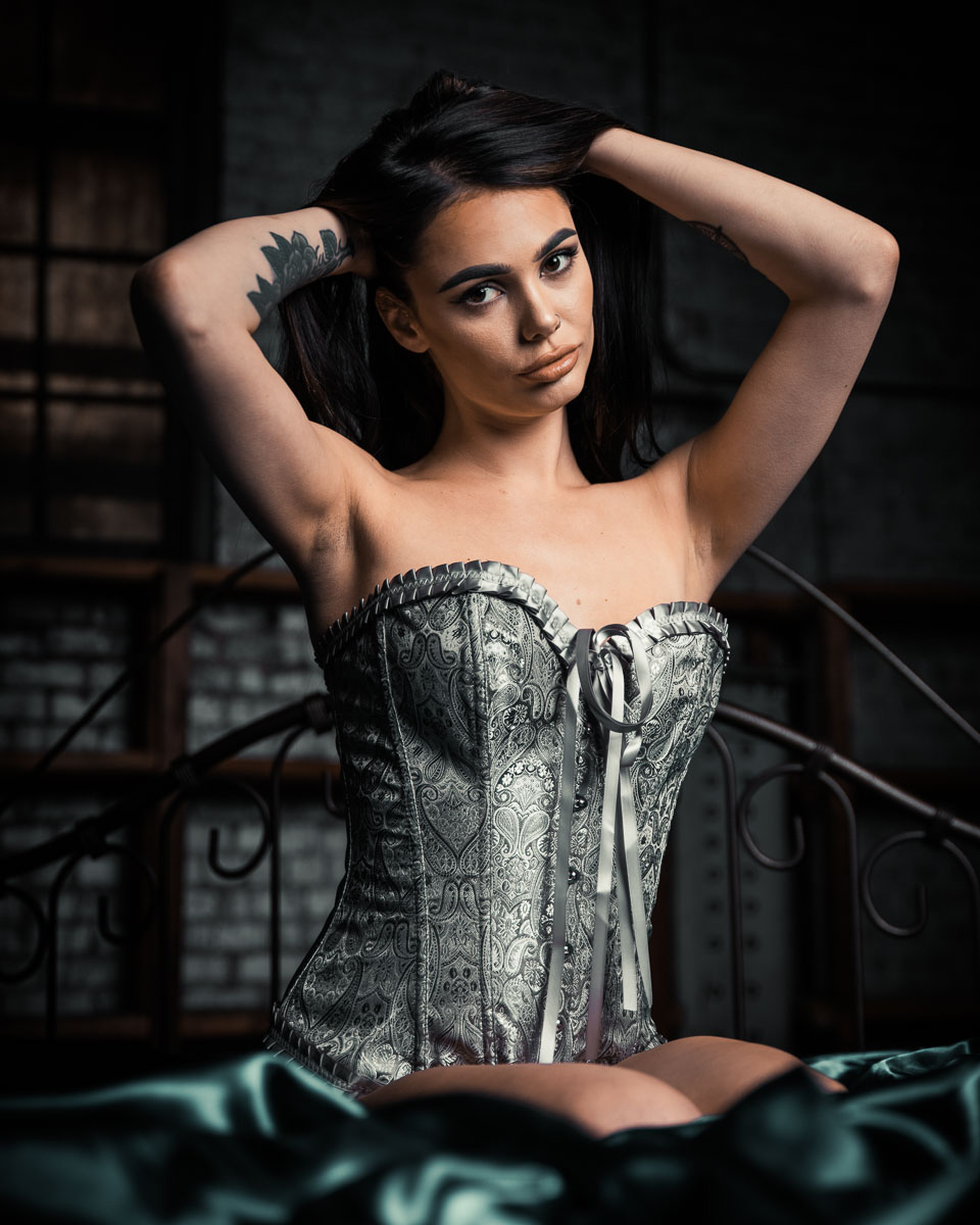 Richmond boudoir photography photo of brunette woman in silver corset kneeling on teal green sheets with hands in hair