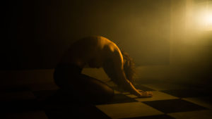 Artistic nude of woman kneeling on the floor bathed in a yellow light coming through the window