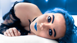 Richmond boudoir photography photo of young woman with blue eyes, blue hair and blue lipstick laying on a white bed