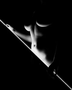 Black and white artistic nude of woman holding a light bar lighting her stomach and the underside of her breasts