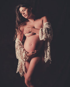 Artistic nude of pregnant woman wrapped in crocheted wrap covering her chest with her arm