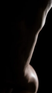 A bodyscape photo of a nude woman on a black background.