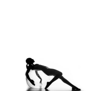 A silhouette of a woman laying on a ball.