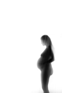 A silhouette of a pregnant woman standing in front of a white wall.