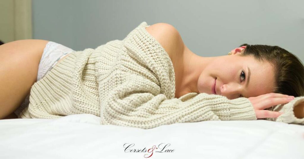 Person in a cream-colored sweater and underwear lying on a white surface, with the logo "Corsets & Lace" visible at the bottom.