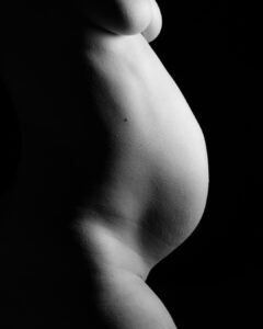 Black and white photo of a pregnant belly in profile against a dark background.