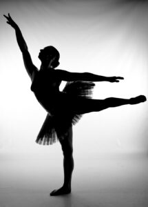 Silhouette of a ballet dancer wearing a tutu, balancing on one leg with the other leg extended backwards and arms outstretched.