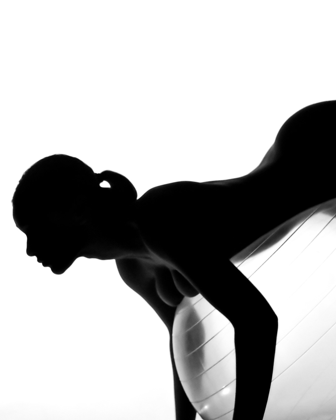 A silhouette of a person with a ponytail leaning forward on an exercise ball against a white background.