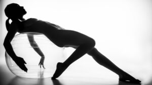 Silhouette of a person reclining with their back arched over an exercise ball, one arm extended and legs stretched out, against a white background.